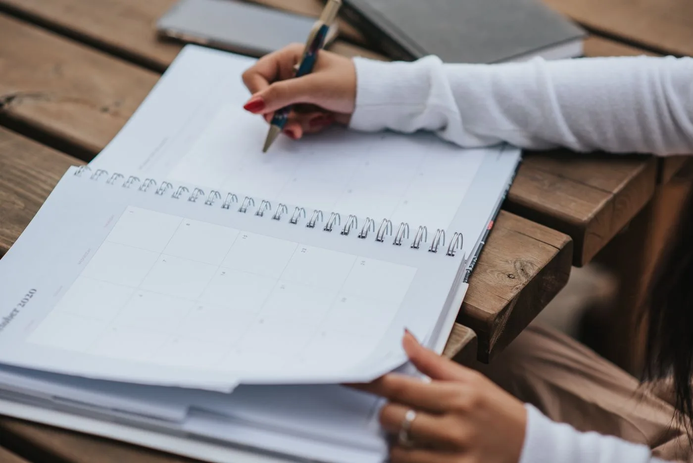 Crop anonymous female student in white blouse writing in notebook while making list of tasks