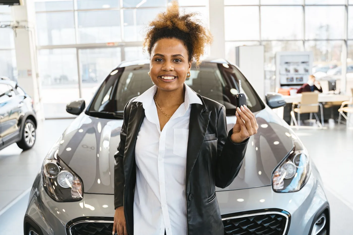 Smiling woman holding car keys in a dealership showroom, celebrating her new car purchase.