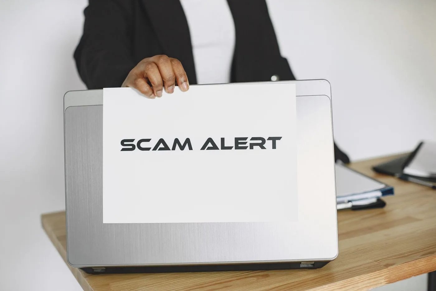 Business person holding a scam alert sign over a laptop, warning against online fraud.
