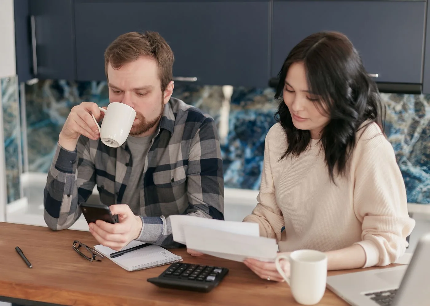 A couple reviewing bills, using a calculator and smartphone, in a modern kitchen.