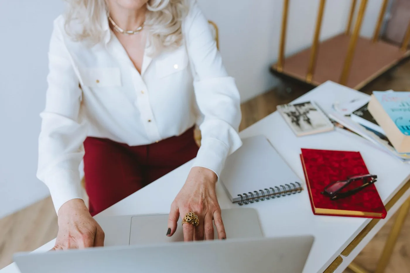 A senior woman using a laptop at a desk with books and a notebook, representing remote work.