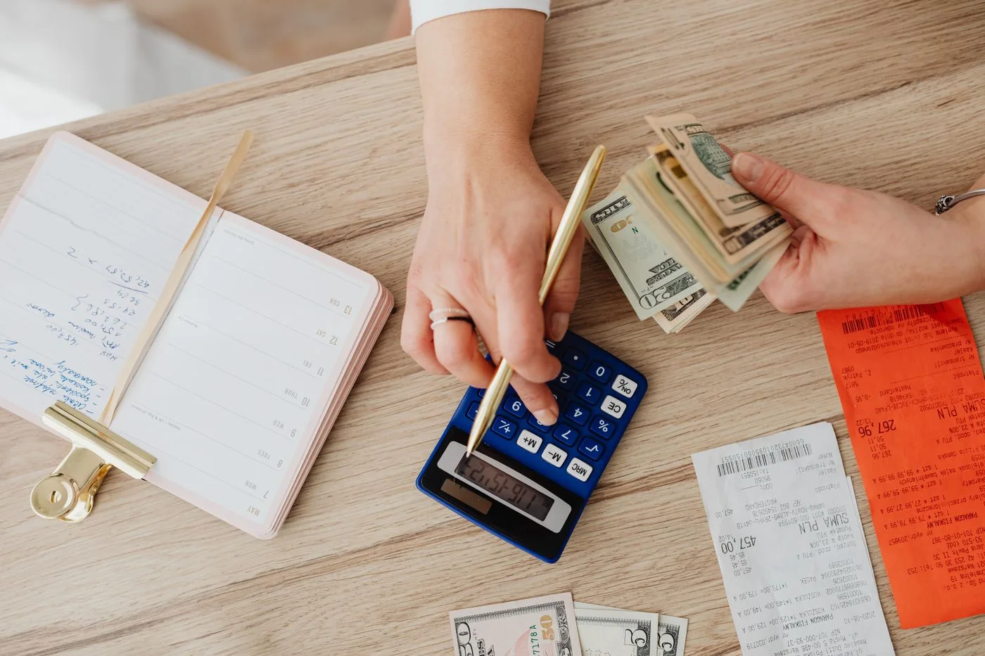 Hands managing finances with calculator, cash, and receipts on a wooden table.