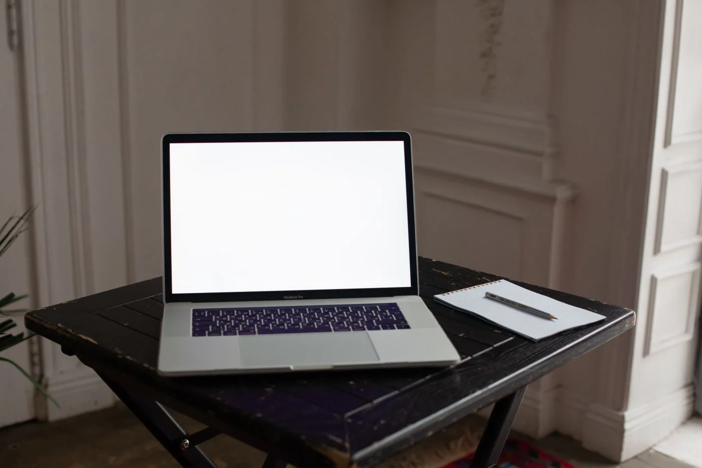 A minimalist home office setup featuring a laptop with a blank screen on a dark wooden table.
