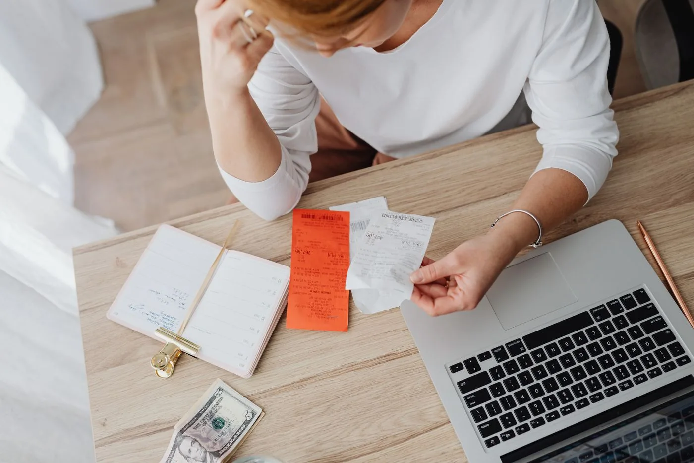 Woman reviewing receipts and planning budget using a laptop and notebook at home to manage expenses.