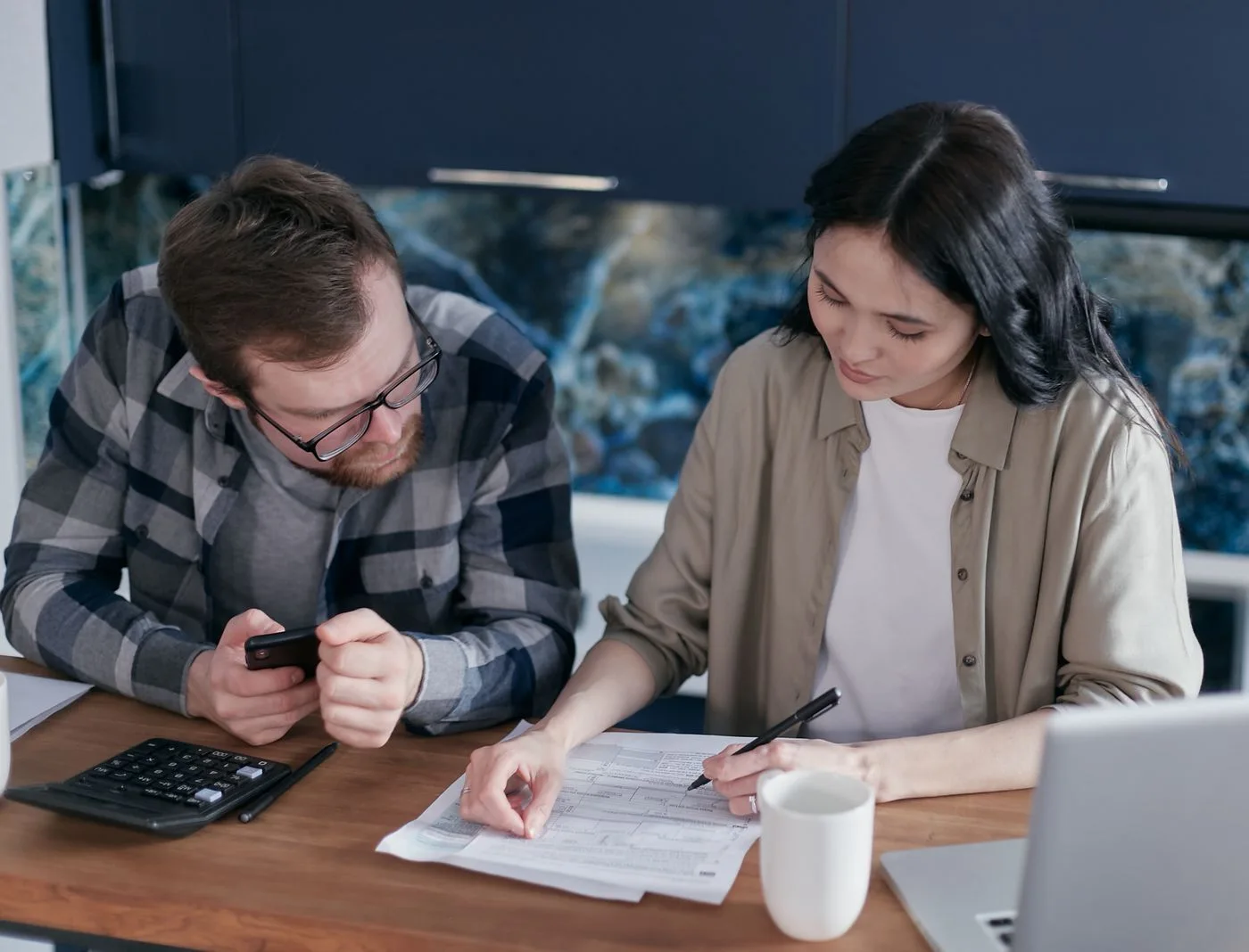 A couple reviewing financial documents at a table, using gadgets like a calculator and phone.