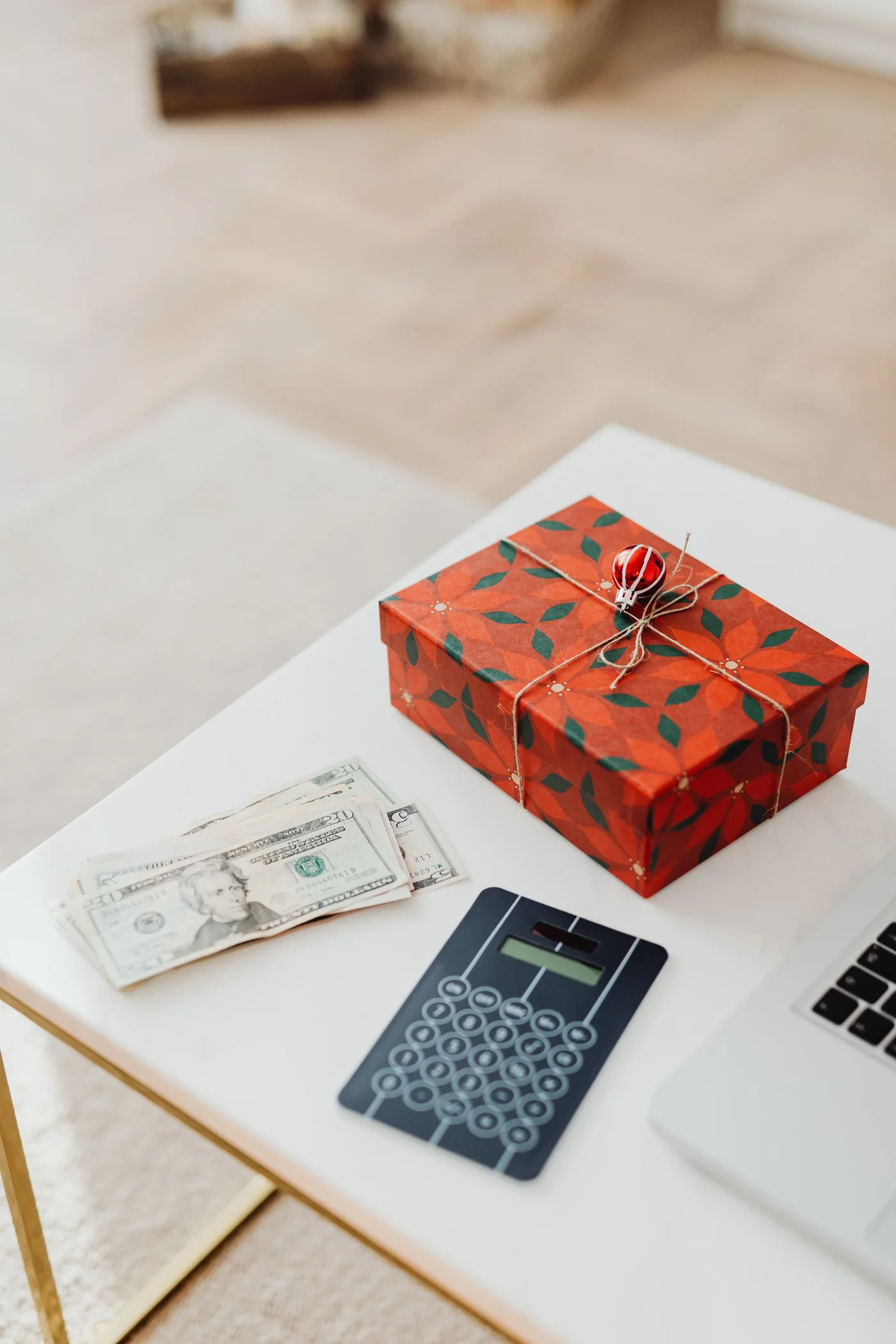 A wrapped gift box with cash and a calculator on a desk, symbolizing financial planning or holiday spending.