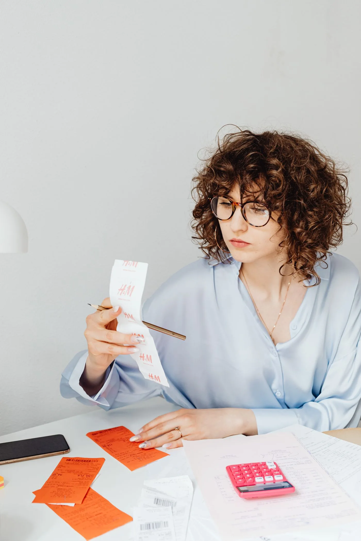 Curly-haired woman examining receipts with a calculator at her desk.