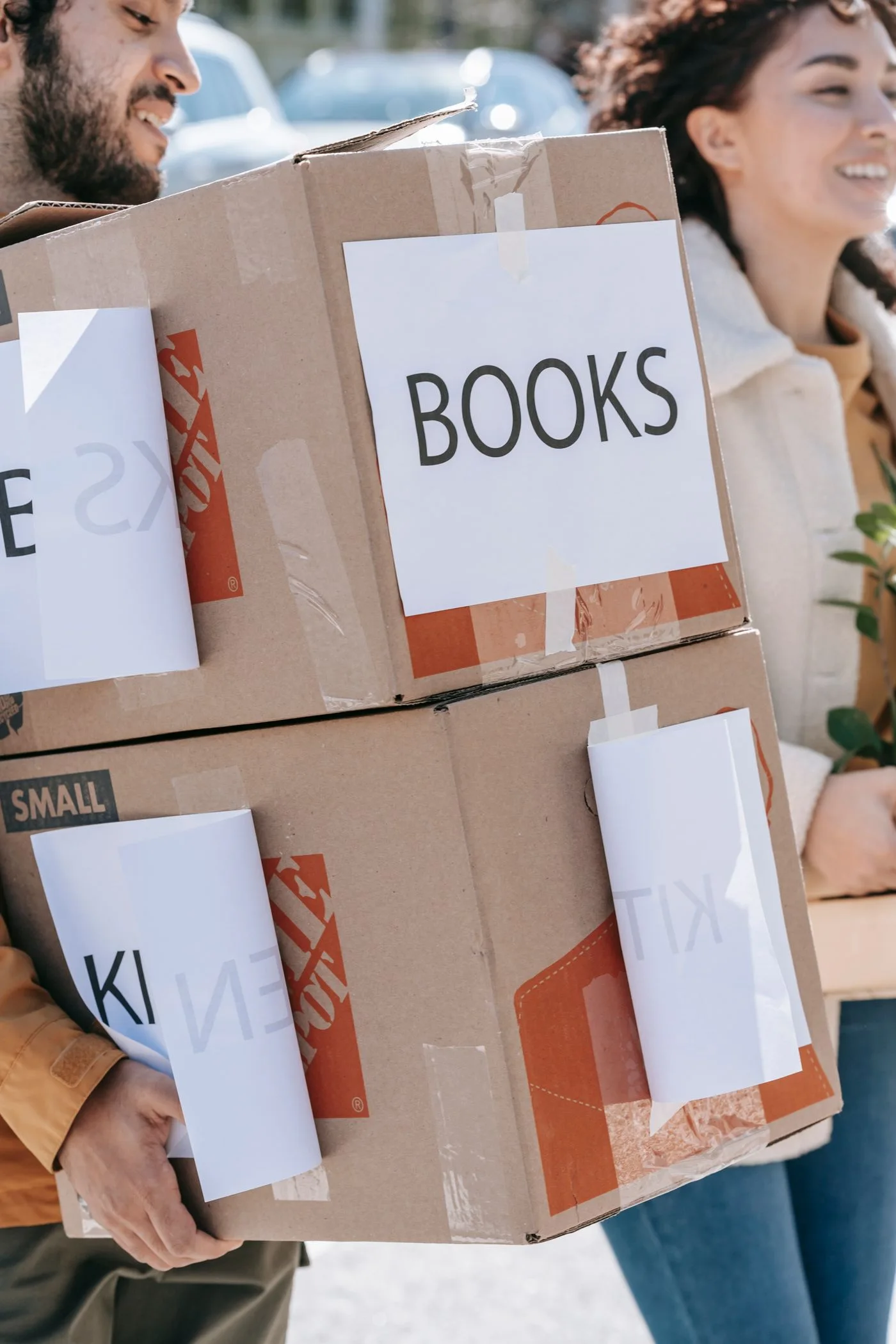 Happy couple moving boxes labeled 'books' and 'kitchen' to their new home, enjoying the process.