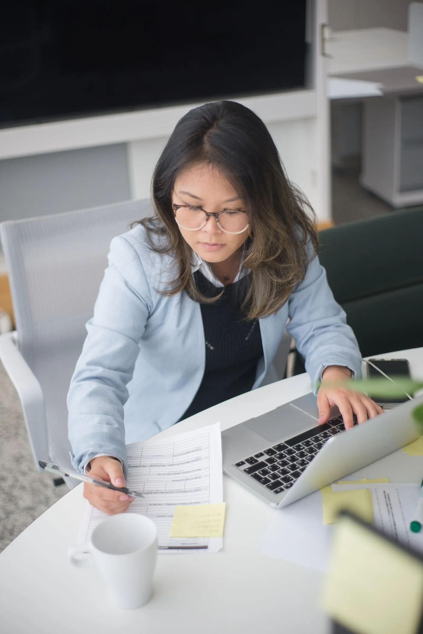 Young businesswoman in eyeglasses working at her office desk with a laptop and documents.